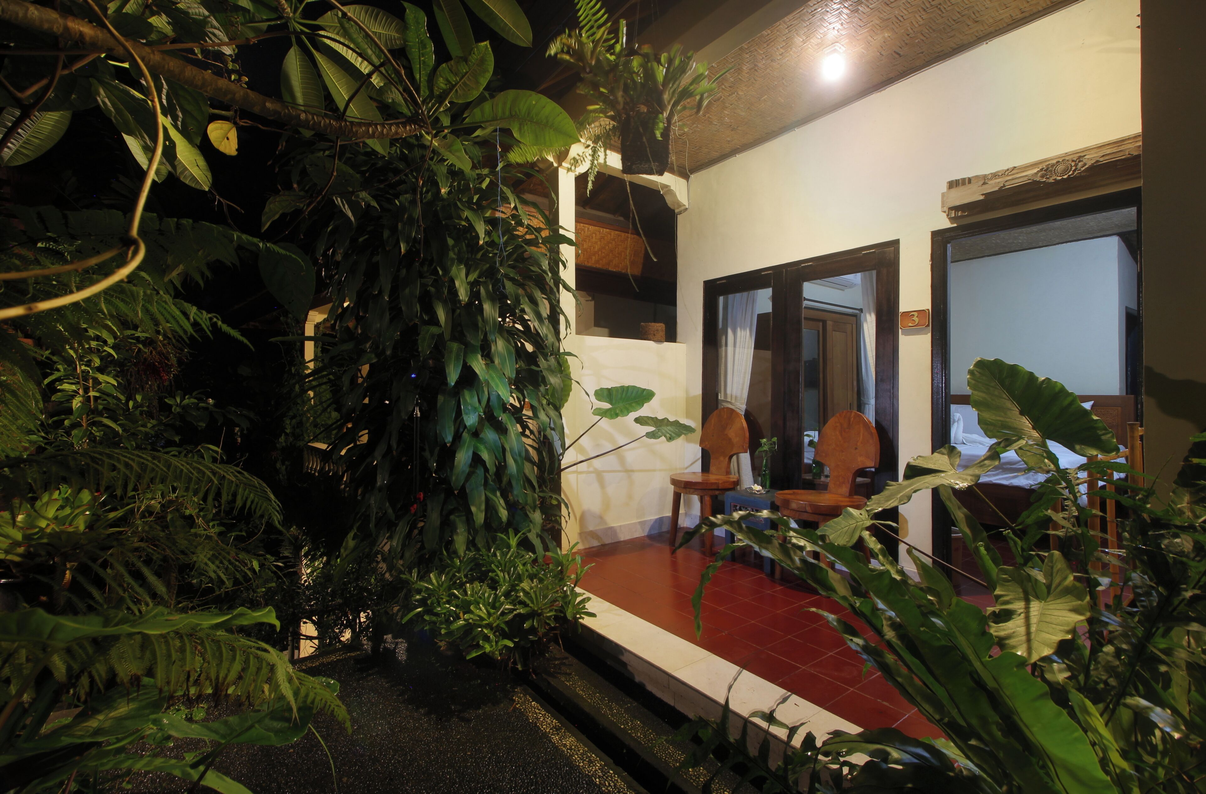 Una habitación con piso rojo, una silla de madera y una planta grande.