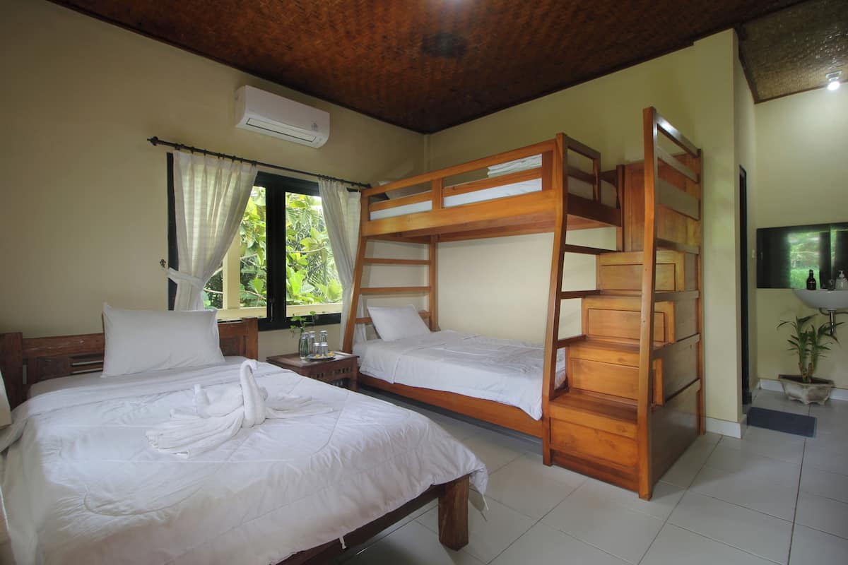A hotel room with two single beds, a wooden bunk bed, a window with curtains, a bedside table with a lamp, and a potted plant.