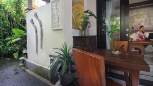 A wooden dining table with chairs, a potted plant, and a Buddha statue. - Sari Gong Guest House, A Trishula Collection (Ubud)