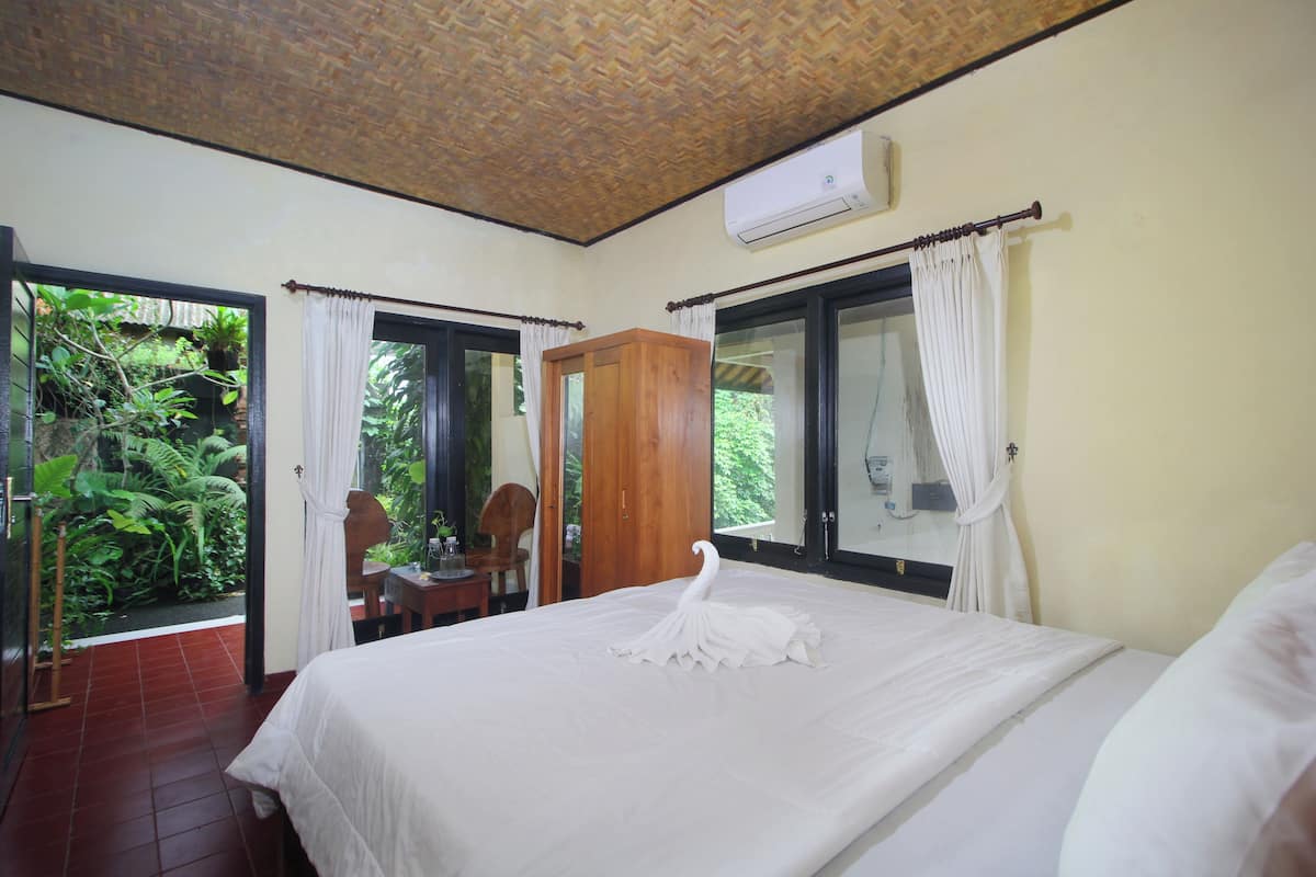 A bedroom with a bed, a wooden wardrobe, a window with curtains, and an air conditioning unit.