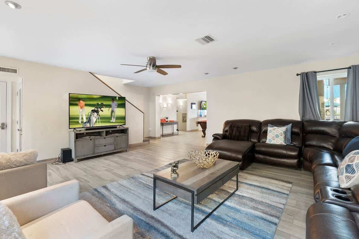 A modern living room with a flat-screen TV, leather sofas, a coffee table, and a ceiling fan.