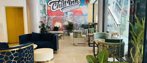 A spacious lounge area with comfortable seating, a colorful mural, and a view of the street outside.