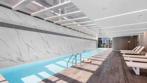 A modern indoor swimming pool with a marble wall, wooden deck, and sunlit ceiling.