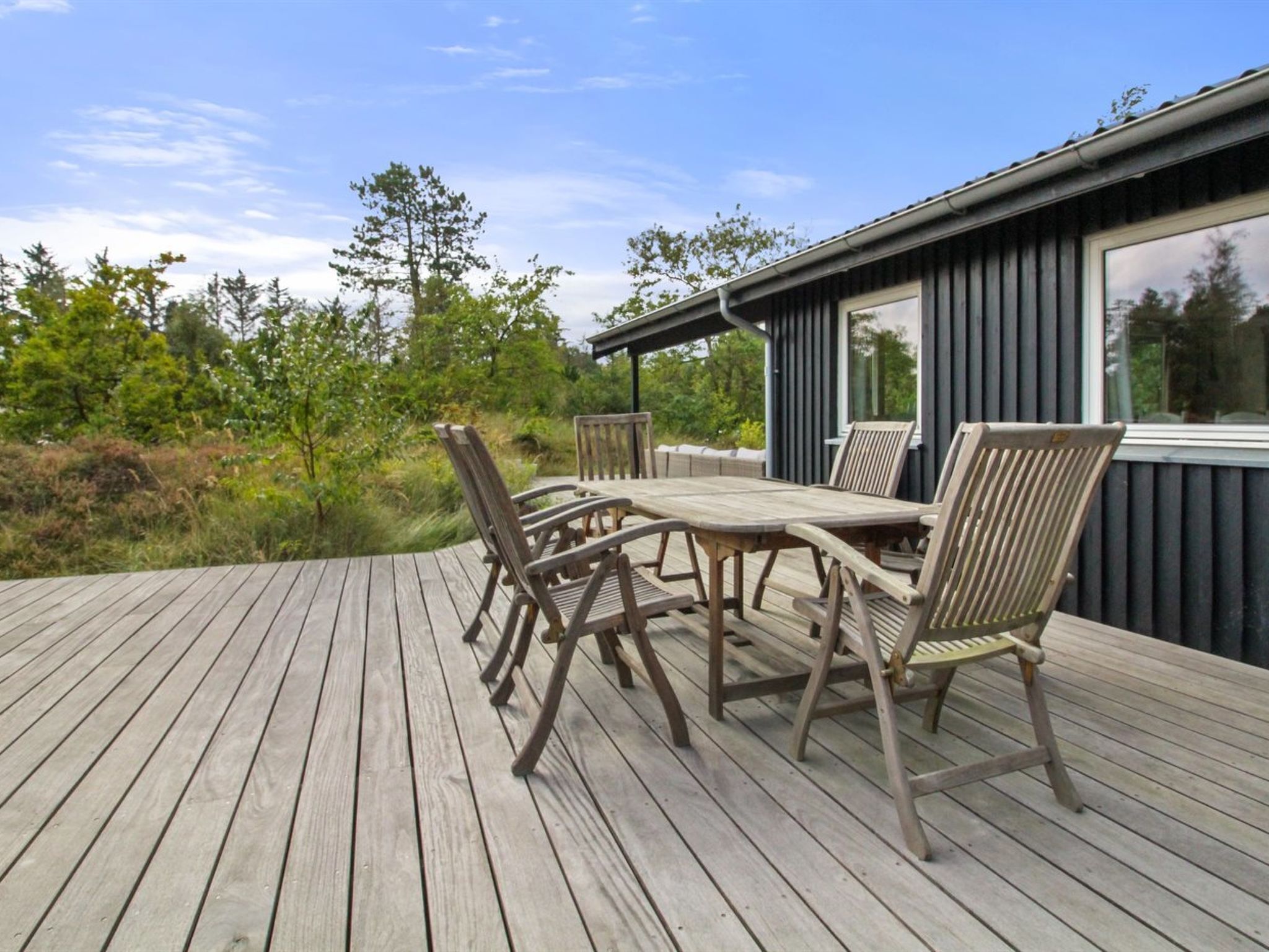 A wooden deck with a table and chairs, surrounded by greenery and trees.