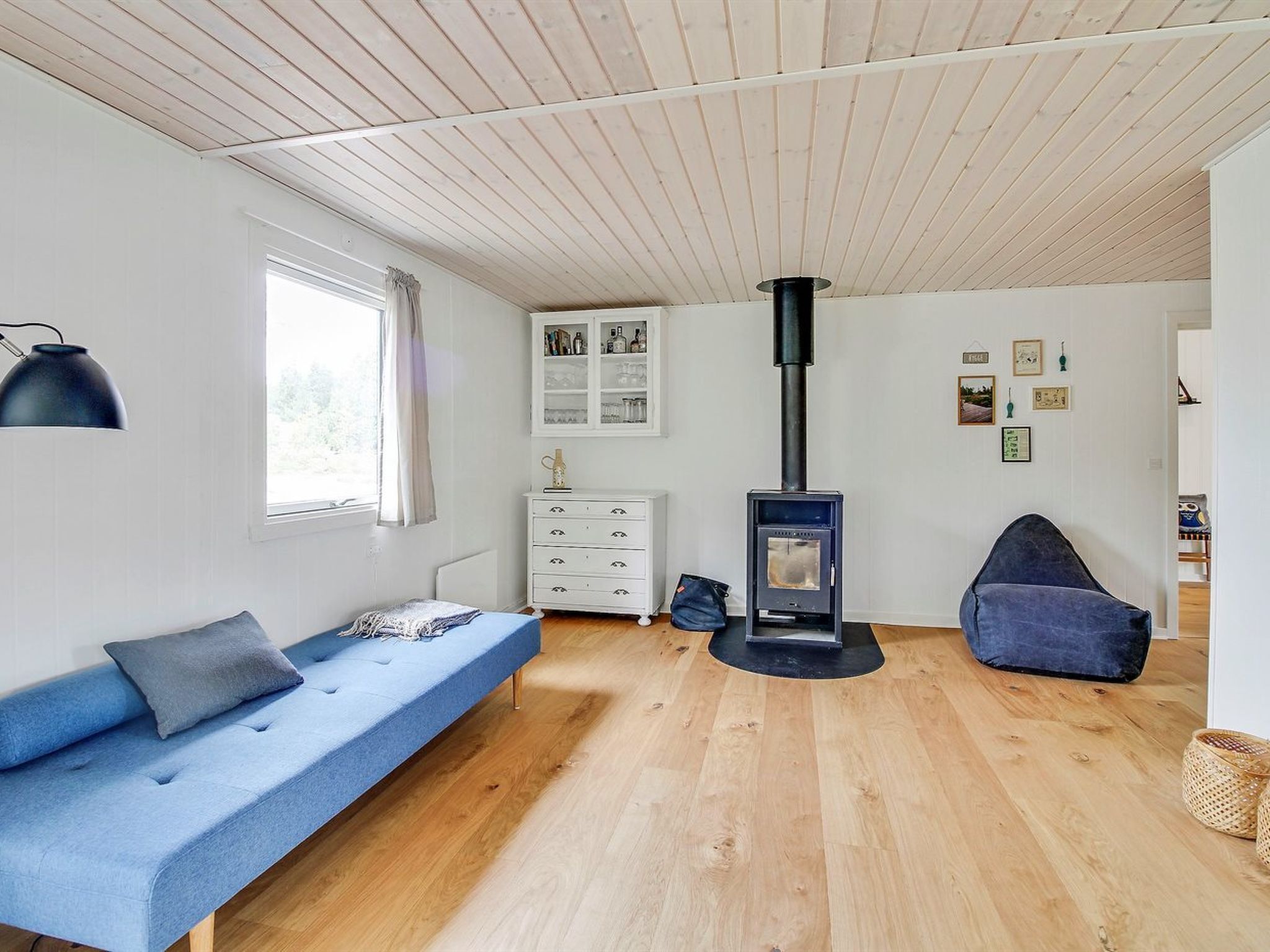 A modern living room with a blue sofa, a white dresser, a black wood-burning stove, and a blue bean bag chair.