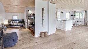 Un vaste espace de vie doté d’un haut plafond, d’un canapé, d’une table à manger et d’un coin cuisine avec des meubles blancs et un luminaire suspendu.