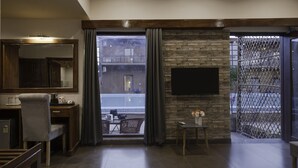 Ett modernt vardagsrum med ett stort fönster, en platt-TV som är monterad på en tegelvägg, en matplats med ett bord och stolar samt ett litet sidobord med en vas med blommor.