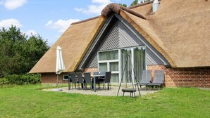 A thatched-roof building with a patio area, a table, chairs, and a swing set. - "Tabithe" - 2.2km from the sea by Interhome (Henne)
