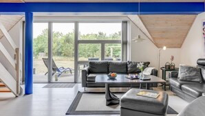 A modern living room with a black leather sofa, a coffee table, and a dining table. There is a large window providing a view of the outdoors. - "Tabithe" - 2.2km from the sea by Interhome (Henne)
