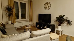 Un salon avec un canapé, une table basse, un téléviseur et deux plantes en pot.