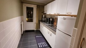Une cuisine étroite avec des meubles blancs, un plan de travail noir et un réfrigérateur blanc.