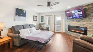 A modern living room with a sofa, a bed, a fireplace, and a mounted TV displaying streaming services. - Wisconsin Dells Escape - Amazing Views - Pools (Wisconsin Dells)