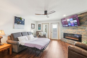 A modern living room with a sofa, a bed, a fireplace, and a mounted TV displaying streaming services. - Wisconsin Dells Escape - Amazing Views - Pools (Wisconsin Dells)