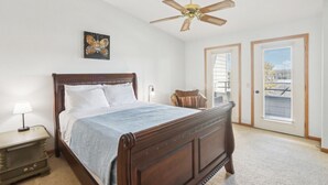 A bedroom with a wooden bed, a ceiling fan, a nightstand, a chair, and a window with blinds. - Wisconsin Dells Escape - Amazing Views - Pools (Wisconsin Dells)
