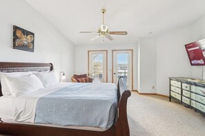 A bedroom with a bed, a ceiling fan, a TV, and a view of the outside.