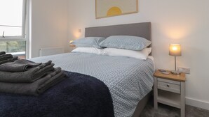 A neatly made bed with patterned bedding, a bedside lamp, and a folded towel on the floor. - River View (Preston)