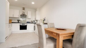 A modern kitchen with white cabinets, a stainless steel range hood, and a dining area with a wooden table and two chairs. - River View (Preston)