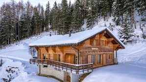 Eine Holzhütte mit Balkon, umgeben von schneebedeckten Bäumen und einer verschneiten Landschaft.