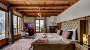 Ein geräumiges Schlafzimmer mit einem großen Bett, einer Holzbalkendecke und Blick auf Berge durch große Fenster.