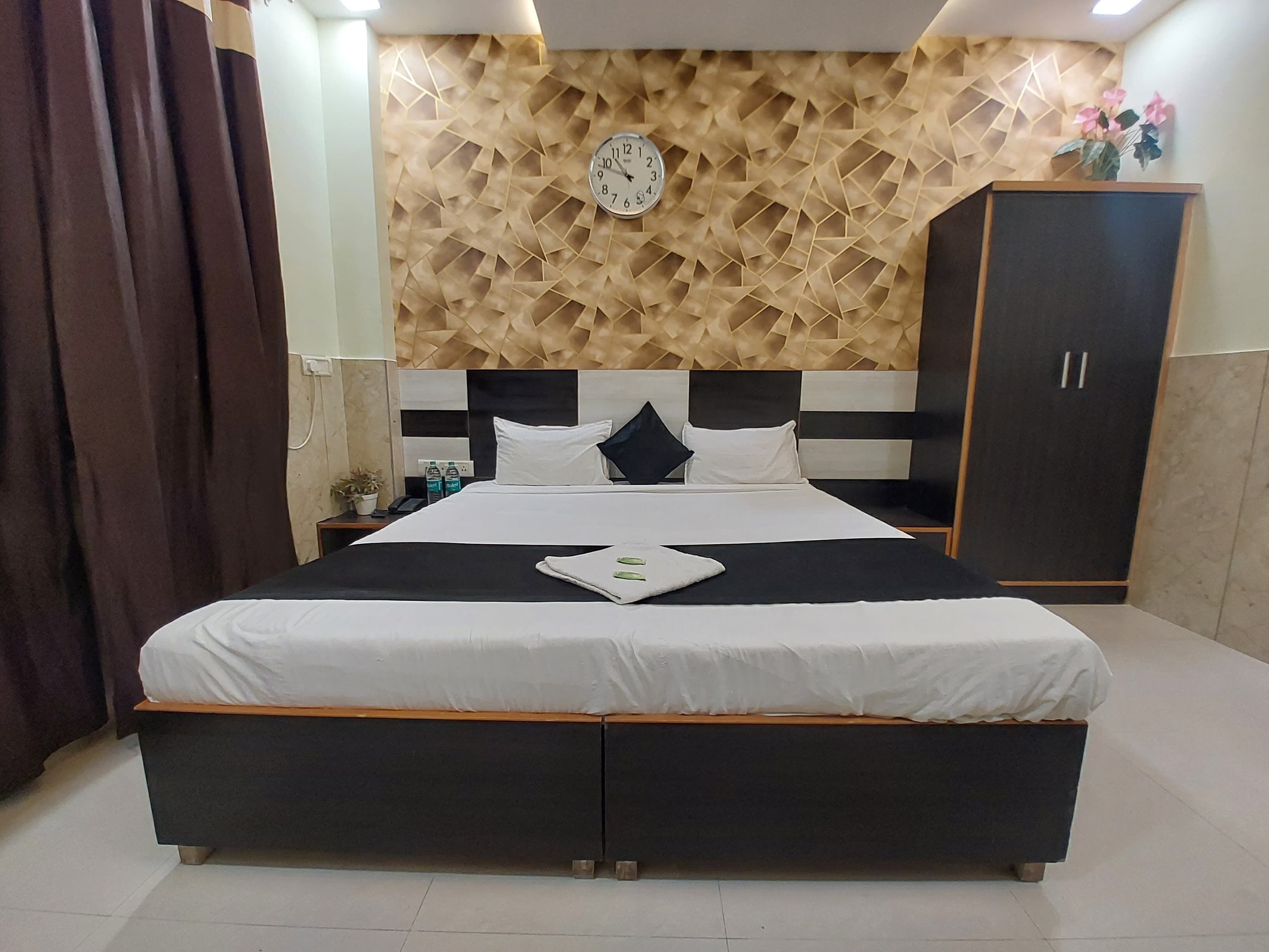 A modern hotel room with a large bed, a wooden textured wall, a clock, and a wardrobe.