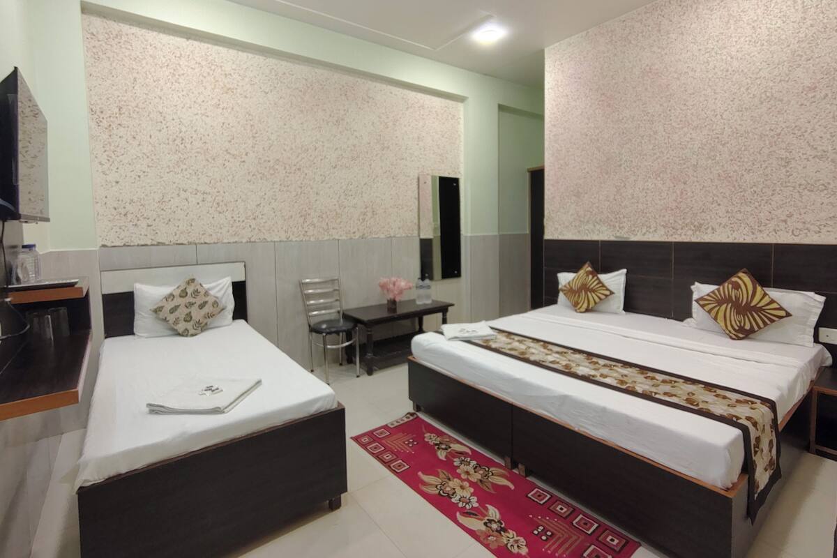 A hotel room with two beds, a desk, a chair, a mirror, and a ceiling fan.