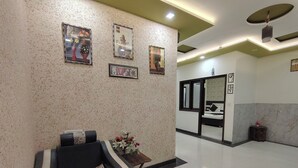 Un moderno vestíbulo de hotel con mostrador de recepción, una zona de estar con sillón de masaje y un espejo grande que refleja la sala.