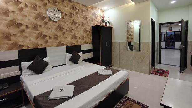 Un dormitorio moderno con una pared de estampado geométrico, una cama con colcha a rayas blancas y marrones, un armario de madera oscura y un ventilador de techo.