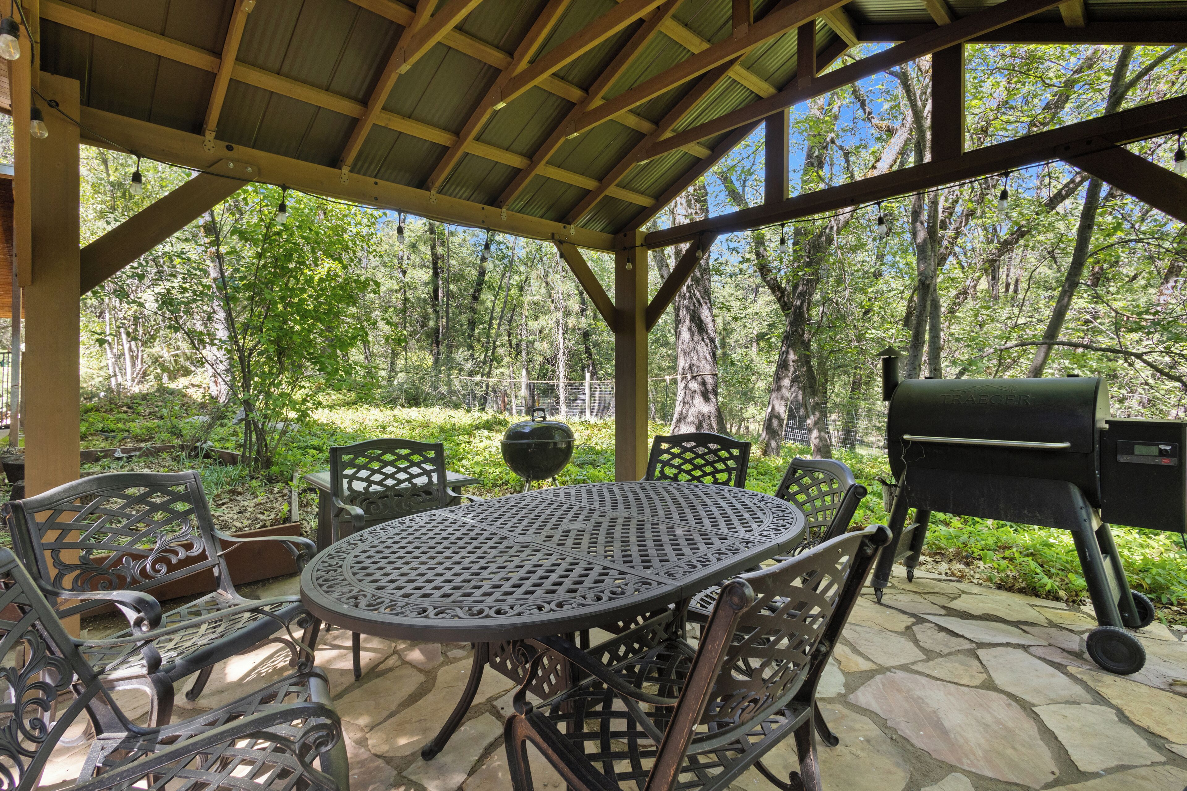Un patio al aire libre con una mesa y sillas de metal redondas, una parrilla y vistas a una zona boscosa.
