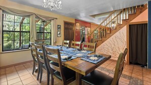 A dining area with a wooden table set for six, surrounded by chairs, a chandelier, and a staircase leading to another level. - Hot Tub Hideaway - Game Room - Near Kirkwood (West Point)