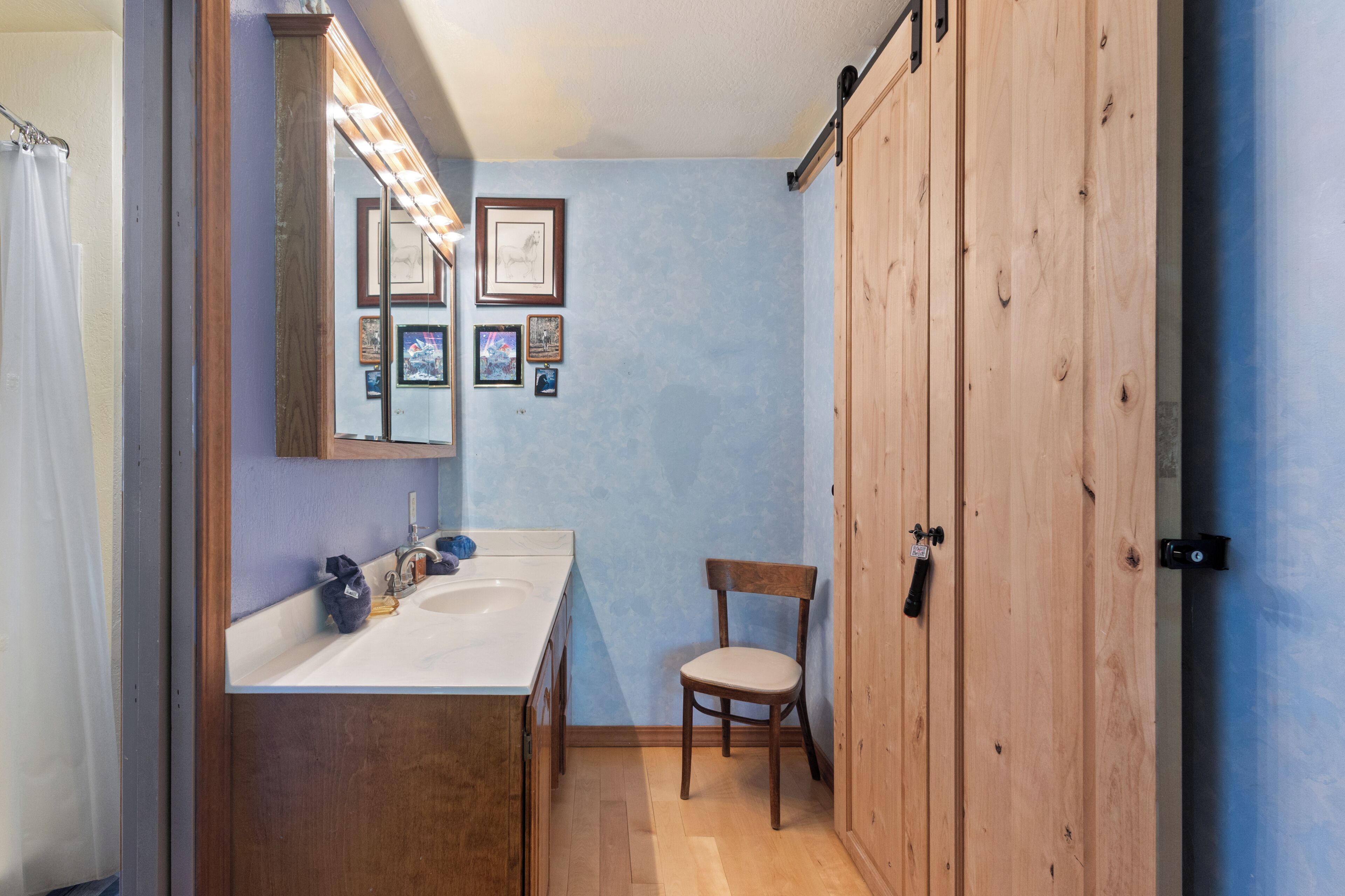 A bathroom with a wooden cabinet, a sink, a chair, and framed pictures on the wall.