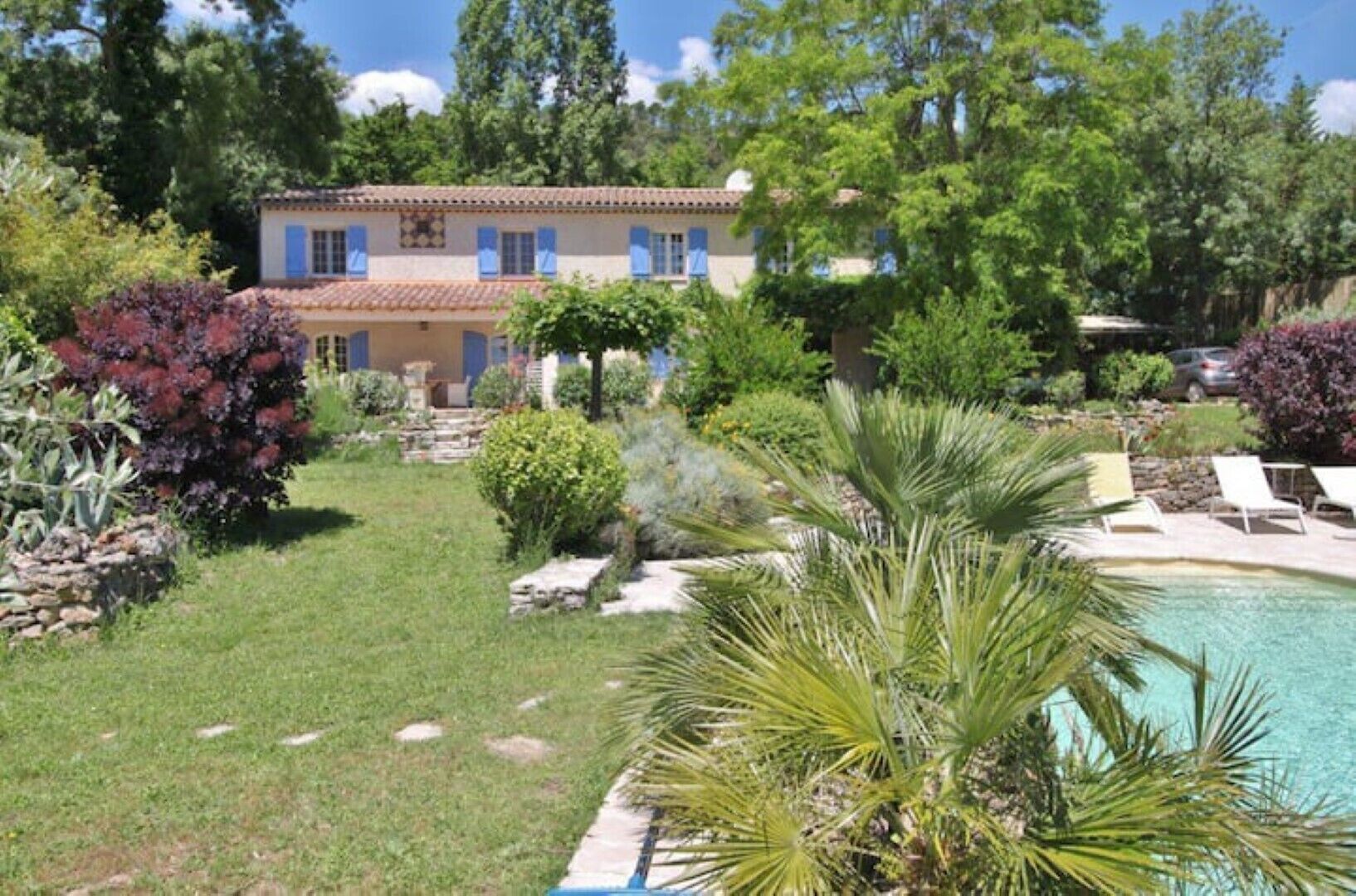 A house with a swimming pool, surrounded by various plants and trees.