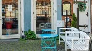 A building with two doors, a small outdoor seating area with a blue table and white chairs, and a brick wall with a green wreath.