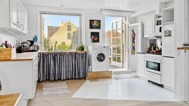 A modern kitchen with white cabinetry, a washing machine, and a large window.
