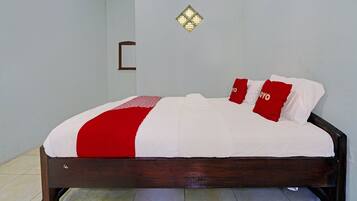 A neatly made bed with a red and white bedspread and matching pillows, a wooden headboard, and a small decorative wall piece above the bed.