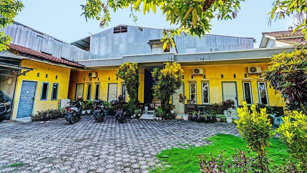 A courtyard with a yellow building, motorcycles, and potted plants.