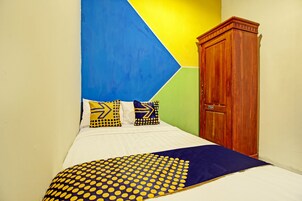 Una cama con colcha celeste y amarilla de lunares, colchón blanco y almohadas con diseños geométricos.