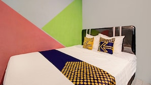 A bed with a white mattress, a blue and yellow polka dot blanket, and two pillows with geometric patterns.