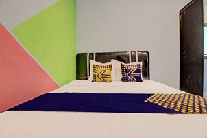 Una cama con sábana blanca, dos almohadas de diseños geométricos y una manta azul y amarilla.