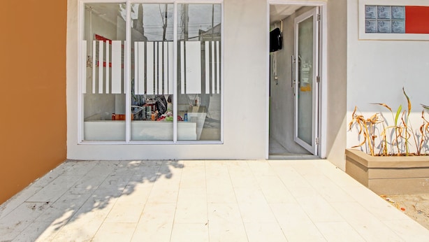 A modern building entrance with large glass doors, a tiled patio, and a small planter with dried plants.