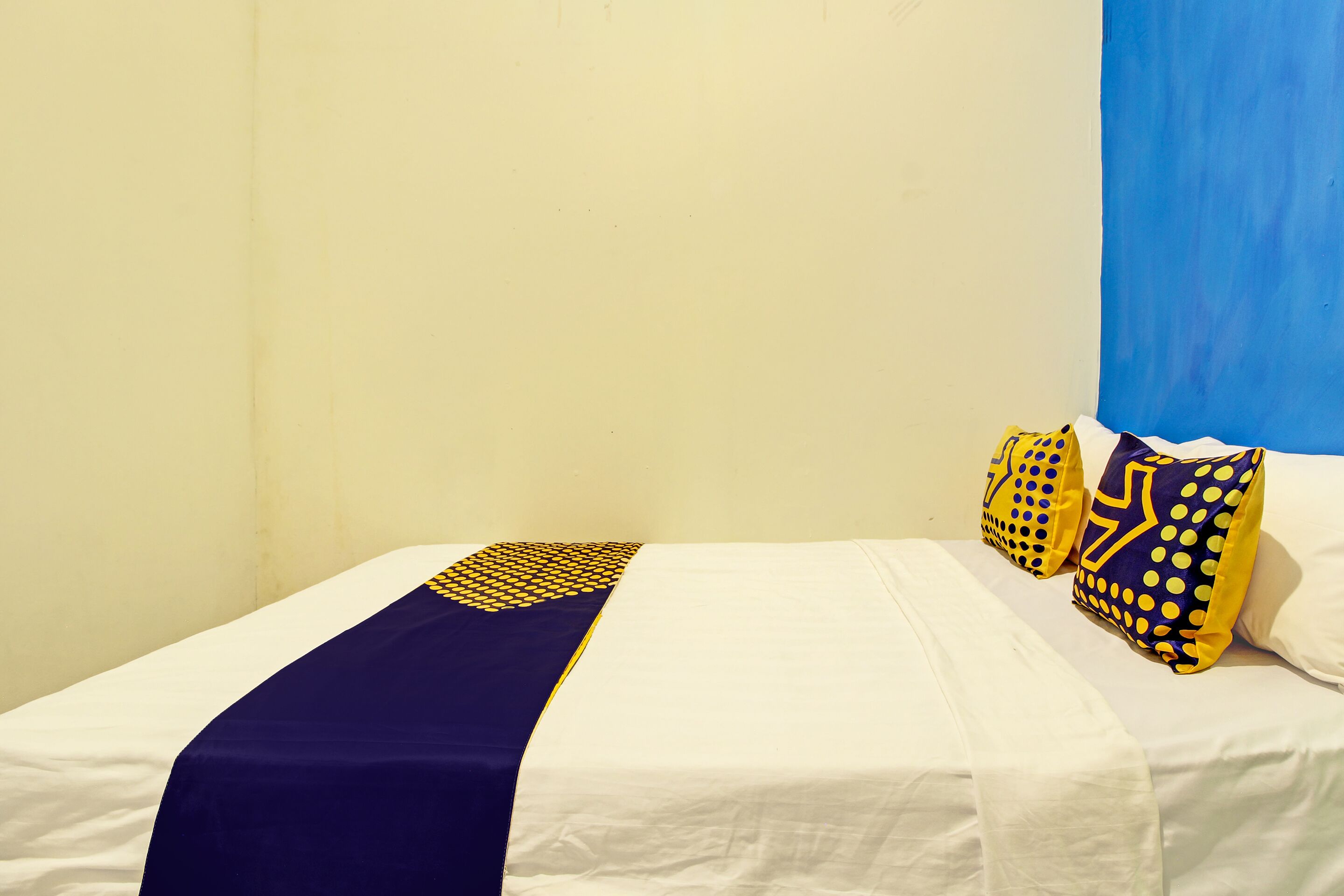 Een bed met wit beddengoed, een blauw-geel sprei en passende kussens.