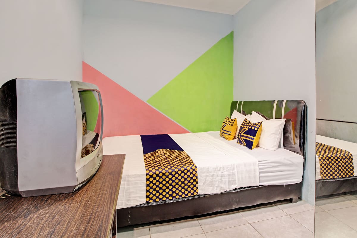 A room with a bed, a television on a wooden table, and a colorful geometric wall design.