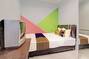 A room with a bed, a television on a wooden table, and a colorful geometric wall design.