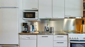 Una cucina compatta con mobili bianchi, un forno a microonde, una macchina per il caffè, un tostapane e un'lavastoviglie.