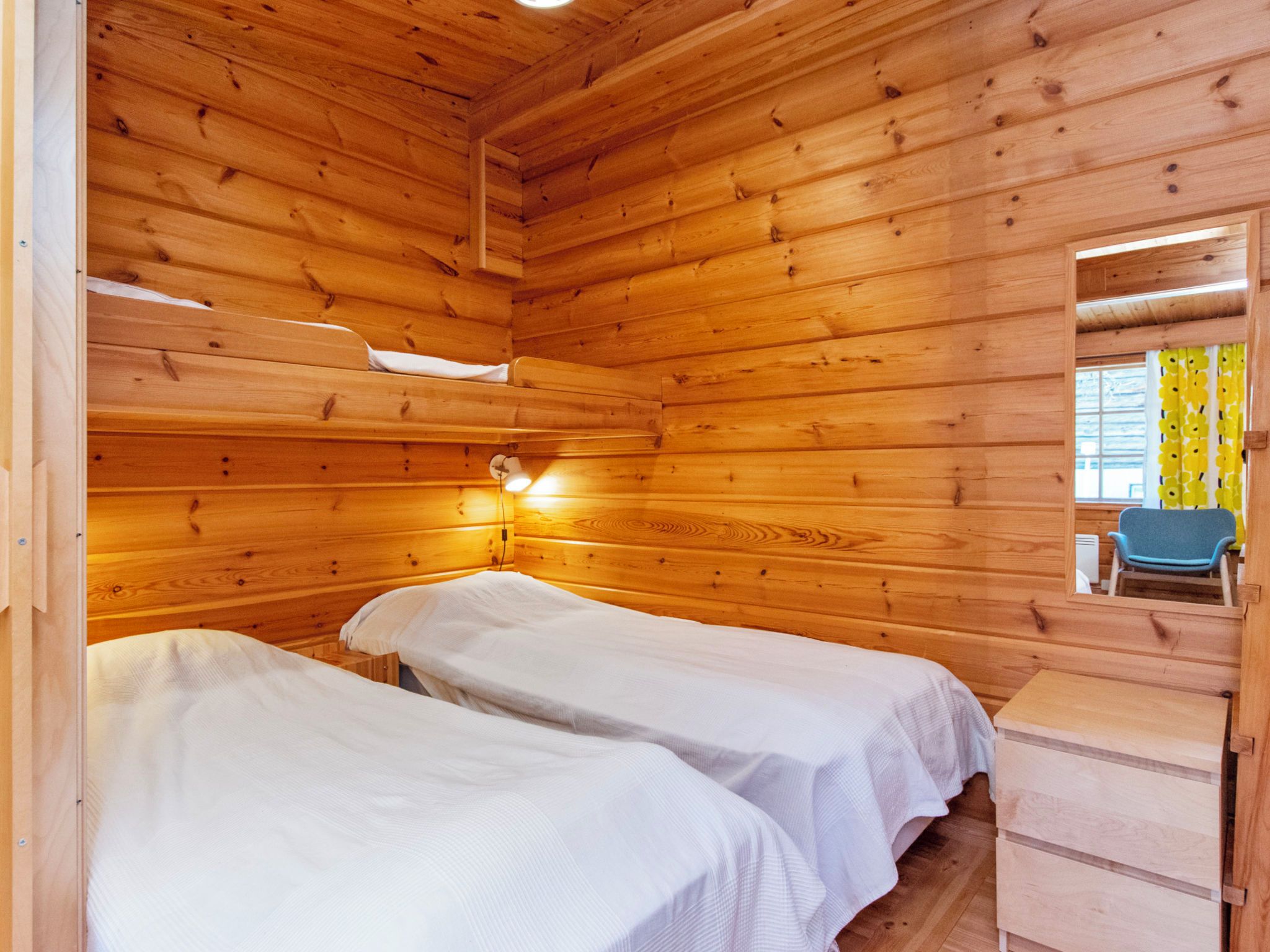 Habitación de cabaña de madera con dos camas, una mesita de noche, un espejo y una ventana con cortinas.