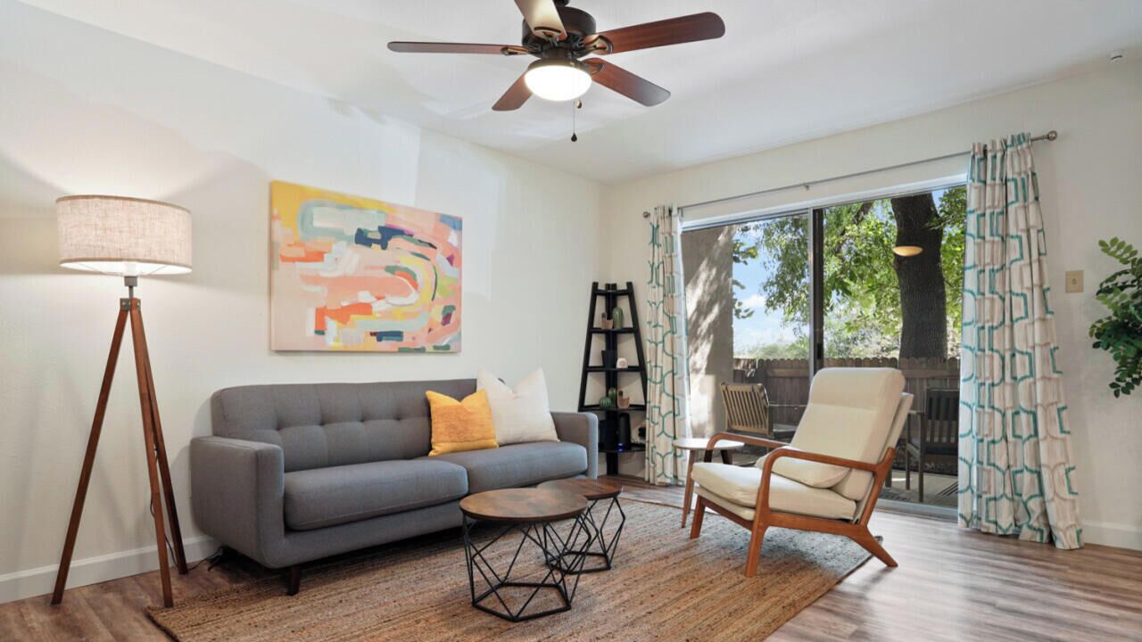 A living room with a gray sofa, two wooden chairs, a coffee table, a floor lamp, and a ceiling fan.