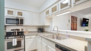 A modern kitchen with white cabinetry, stainless steel appliances, a double sink, and a flat-screen TV mounted above the sink. - Hart #206 xxxxxxxxxx (Austin)