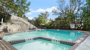 A rectangular swimming pool with a stone wall on one side and a grassy area with a bench and umbrella on the other. - Hart #206 xxxxxxxxxx (Austin)