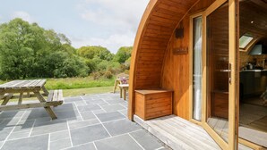 A wooden cabin with a stone patio, a wooden table, and a bench. - Llugwy Pod (Llanrwst)