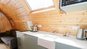 A compact kitchenette with a wooden ceiling, a white countertop, a sink, a toaster, and a kettle. - Llugwy Pod (Llanrwst)