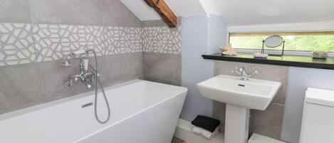 A modern bathroom with a freestanding bathtub, a pedestal sink, and a window above the sink.